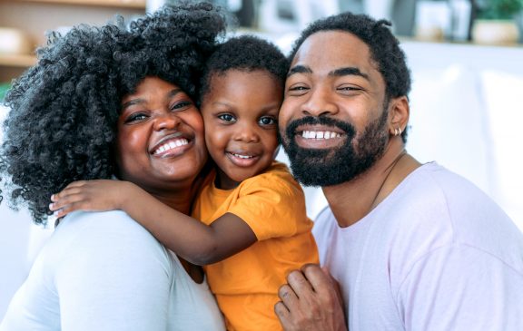 Shot of cheerful mother and father embracing their cute boy while sitting on the sofa in living room.