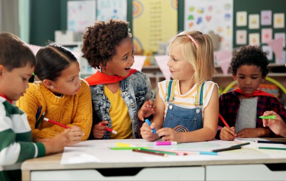 Happy children, drawing and coloring with classmates in kindergarten for fun activity in classroom. Group of young elementary kids sketching colorful paper, poster or sign for learning or development