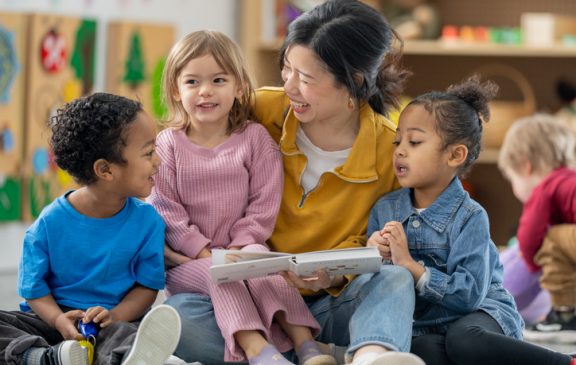 Group of young children sitting with their teacher actively engaged in a story session, fostering learning and collaboration in a vibrant preschool classroom environment.