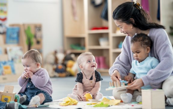 An attentive caretaker plays with children in a colorful nursery setting, fostering engagement and social interaction.