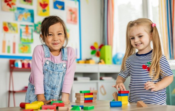 Happy little children are sitting on the floor in the kindergarten and playing with toys.